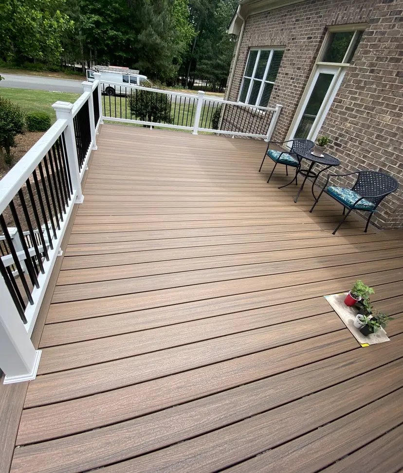 Long composite deck with brown boards and a white railing beside a brick home