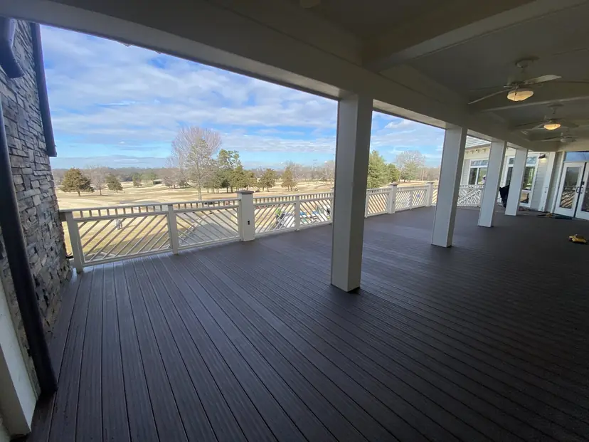 Long covered porch with a dark deck, white rail and a golf course view