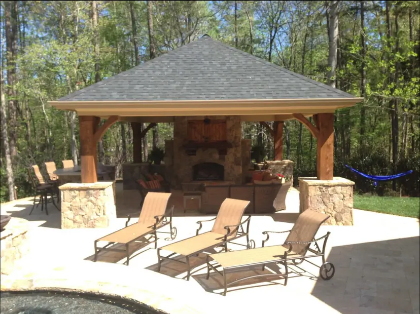 Cabana with a stone fireplace and a built-in kitchen beside a patio with lounge chairs