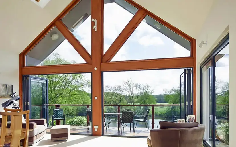 Gabled sunroom with a wall of bi-fold doors folded open onto a deck by the water