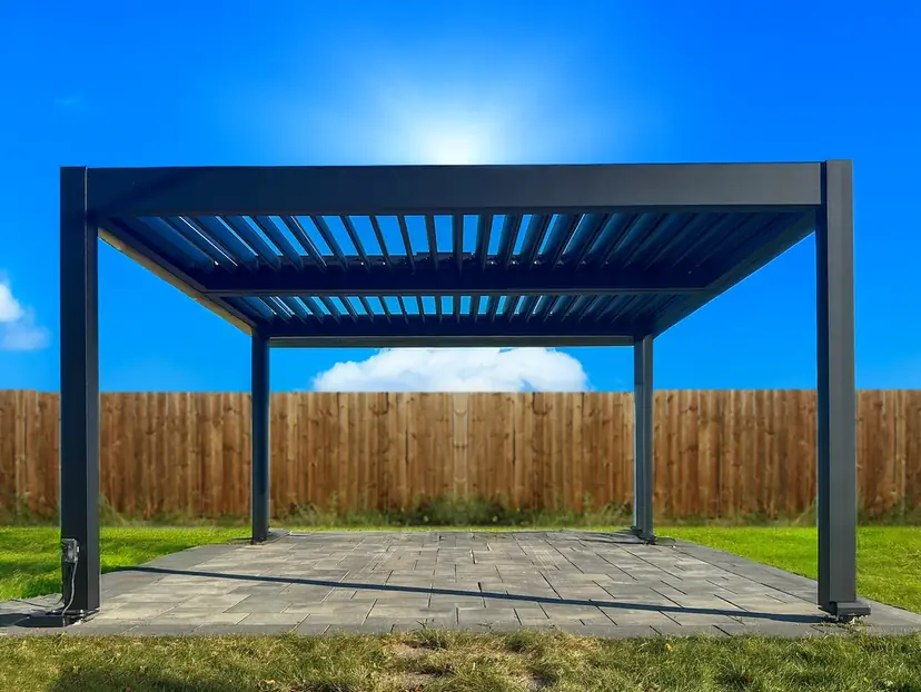 Black louvered pergola standing on four posts on a lawn beside a wood fence